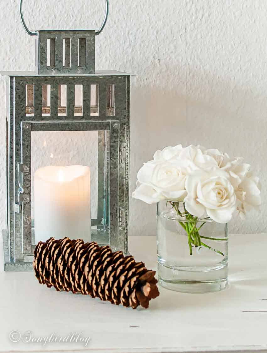 galvanized metal lantern with burning candle white roses and pinecone