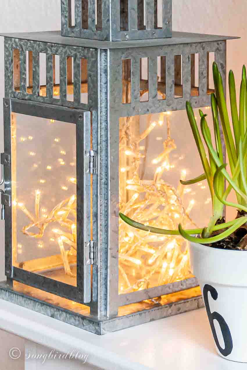 galvanized lantern with fairly lights inside on a spring mantel